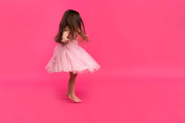 Cute little girl dreams of becoming a ballerina. Little Dancing Girl. Studio Shoot Over Pink Background.