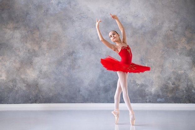 A cute little girl dreams of becoming a professional ballerina A girl in a bright red tutu on pointe shoes dances in the hall Vocational school student