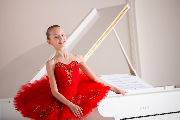 Милая маленькая девочка мечтает стать профессиональной балериной В белой комнате стоит за роялем в ярко-красной пачке Ученица ПТУ