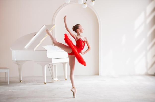 A cute little girl dreams of becoming a professional ballerina In a white room next to a piano a girl in a bright red tutu is dancing on pointe shoes Vocational school student