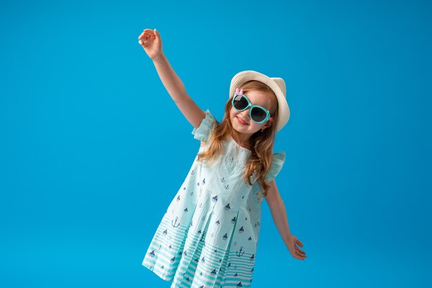 Cute little girl in a dress, hat and sunglasses poses