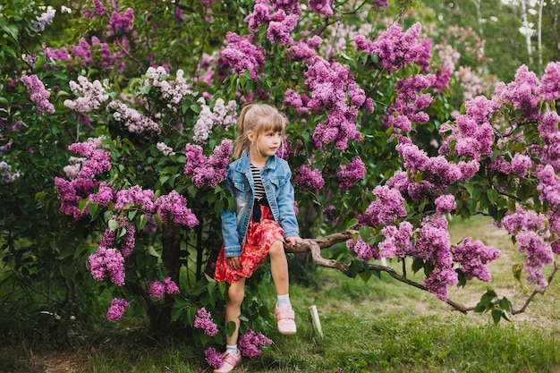 Милая маленькая девочка в платье смеется в весеннем парке возле сирени ребенок пахнет сиренью