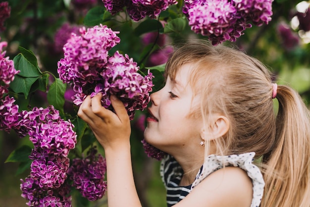 Cute little girl in dress laughing in spring park near lilac child smells lilac