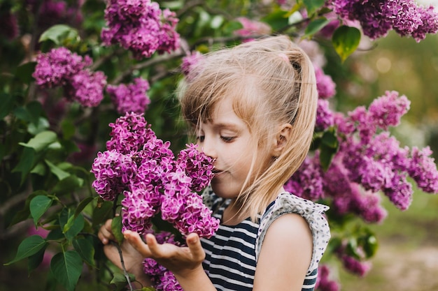 Cute little girl in dress laughing in spring park near lilac child smells lilac