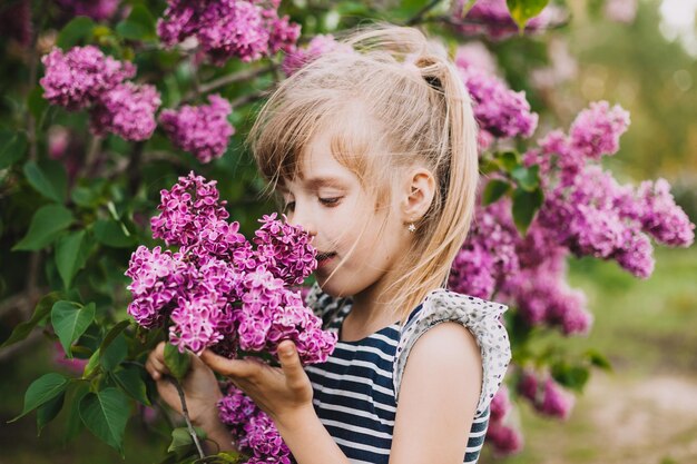 Cute little girl in dress laughing in spring park near lilac child smells lilac