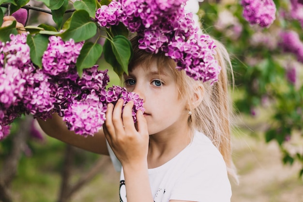 Bambina sveglia in vestito che ride nel parco di primavera vicino al bambino lilla odora di lillà