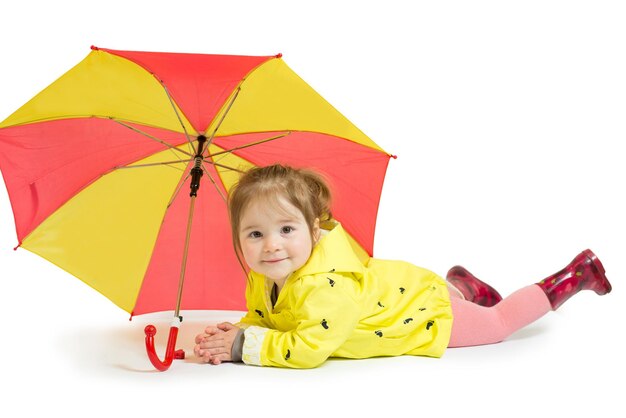 Cute little girl dressed in a yellow raincoat and with a colored umbrella on a white background