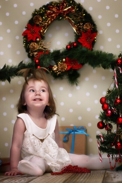 Cute little girl dresses up Christmas tree on the floor in the room