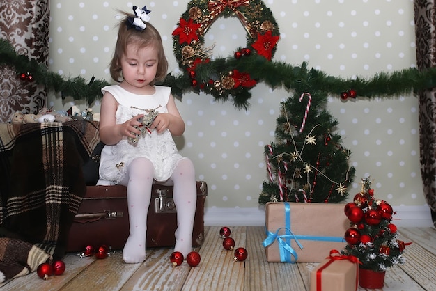 Cute little girl dresses up Christmas tree on the floor in the room