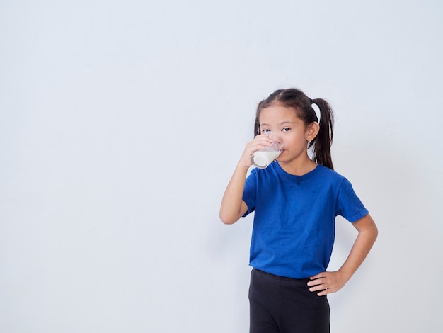 Cute little girl drinking milk from glass on light