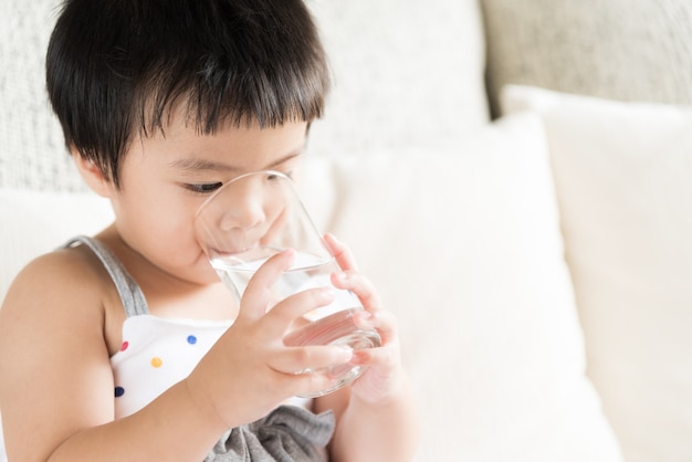 Cute little girl drinking water on sofa at home. Health care concept.