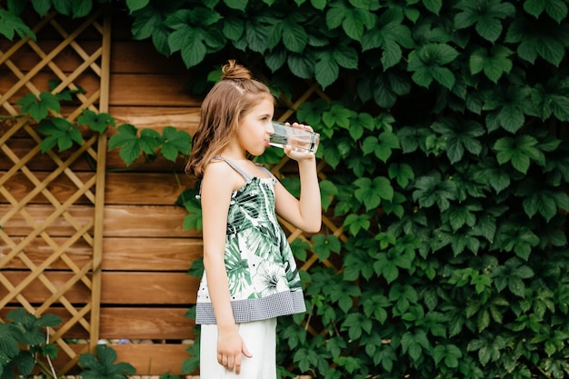 Фото Милая маленькая девочка пьет воду. лето