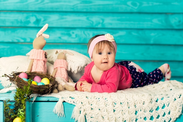 Милая маленькая девочка в пасхальных украшениях с голубой деревянной стеной на предпосылке.