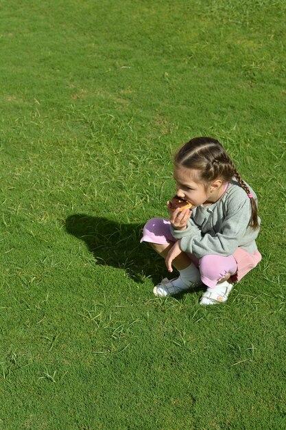 Cute little girl eating donut on green grass