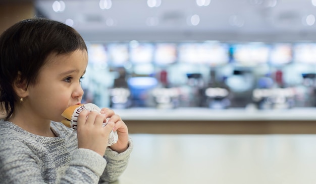 Cute little girl eating a hamburger in the Fast food