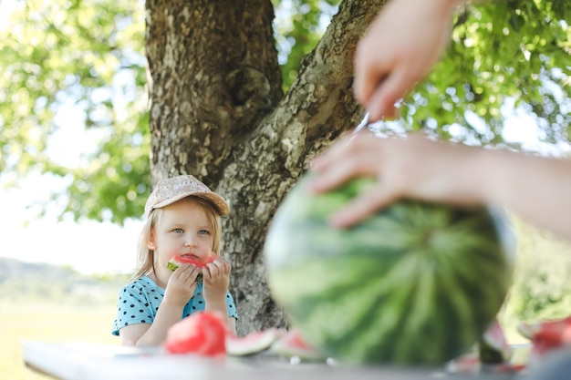 Bambina sveglia che mangia anguria all'aperto in estate bambino e anguria in estate