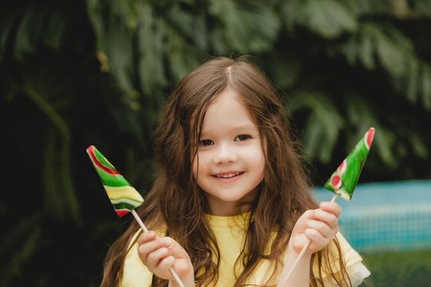 수박 모양의 막대 사탕을 먹는 귀여운 소녀 식물원에서 막대 사탕을 가진 아이