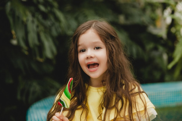 Cute little girl eating a watermelon shaped lollipop Child with lollipops in the botanical garden