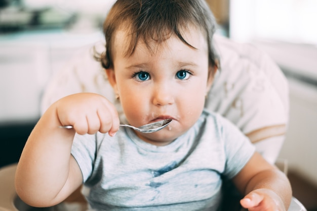 高い椅子で日中にキッチンでヨーグルトを食べるかわいい、小さな女の子