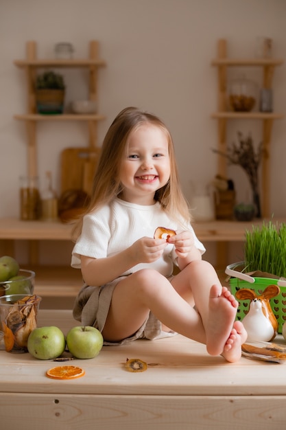 Cute little girl eats natural pastille at home in a wooden kitchen.