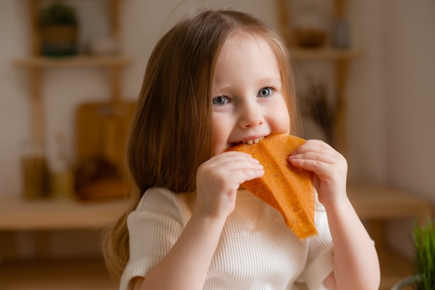 Cute little girl eats natural pastille at home in a wooden kitchen.