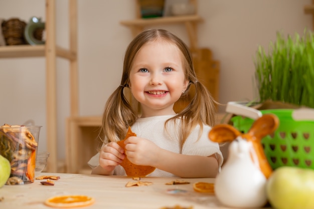 Cute little girl eats natural pastille at home in a wooden kitchen.