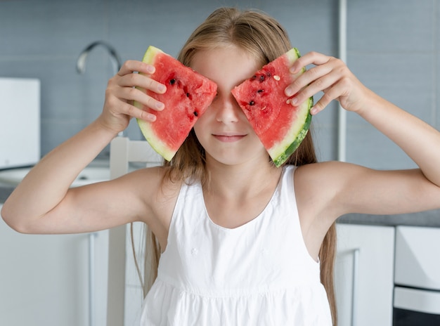 Cute little girl eats a watermelon in the kitchen