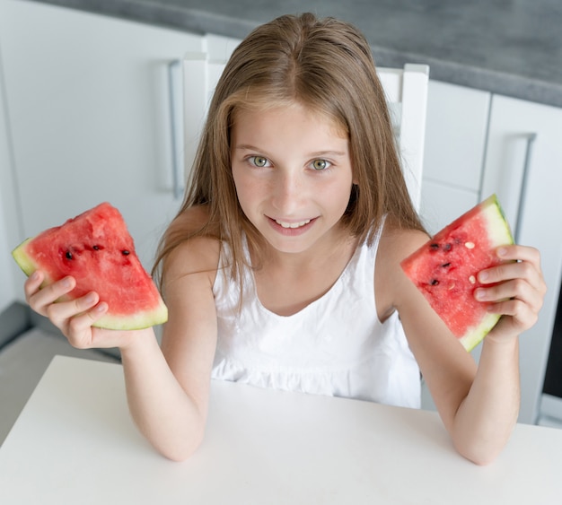 Cute little girl eats a watermelon in the kitchen