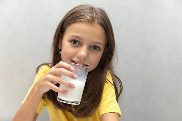 Милая маленькая девочка наслаждается стаканом молока и улыбается на сером фоне