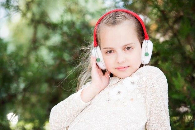 Cute little girl enjoying music using headphones at summer day