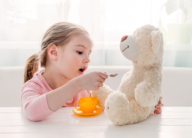 Cute little girl feeding toy teddy bear