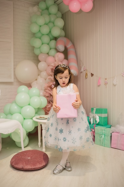 A cute little girl in a fluffy dress stands with a gift in the New Year decorations