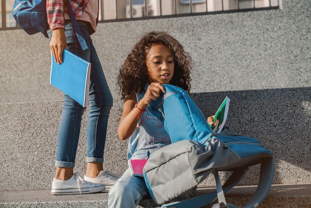 Cute little girl folding her school backpack outdoors