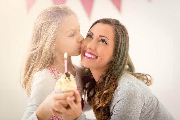 彼女の笑顔のお母さんのためにキャンドルで小さなカップケーキを与えるかわいい女の子。セレクティブフォーカス。背景、お母さんに焦点を当てます。