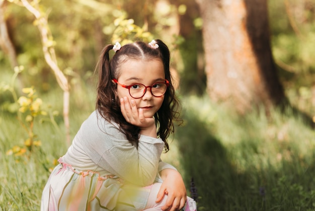 A cute little girl in glasses in nature on a sunny day