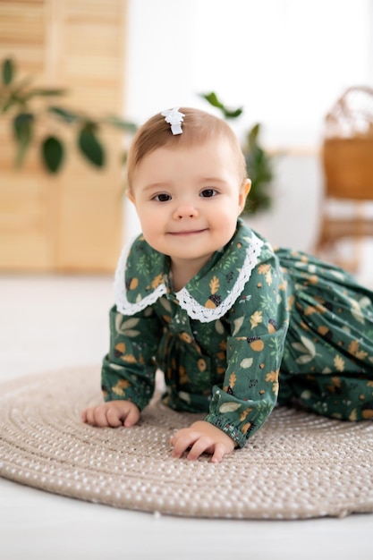 緑の綿のドレスを着たかわいい女の子が家のリビングルームでクロールし、カメラの笑顔を見て、赤ちゃんは大きな肖像画を歩くことを学びます