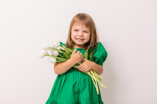 Bambina carina in un abito di cotone verde con un mazzo di tulipani su uno sfondo chiaro 8 marzo festa della mamma spazio banner per il testo