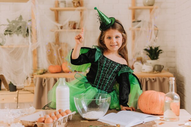 Cute little girl in a green Halloween costume of a witch or fairy prepares a pumpkin pie