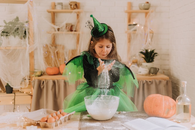 마녀나 요정의 녹색 할로윈 의상을 입은 귀여운 소녀가 호박 파이를 준비합니다