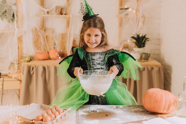 Cute little girl in a green Halloween costume of a witch or fairy prepares a pumpkin pie