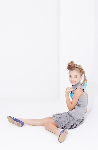 Cute little girl in grey dress sits white studio background.