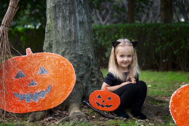 Cute little girl in halloween costume sitting near pumpkin decoration