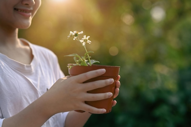 ぼやけた緑の自然の背景に鉢植えの植物を保持しているかわいい女の子の手アースデイエコロジーコンセプト