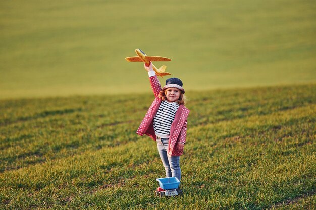 Cute little girl have fun with toy plane on the beautiful green field at sunny daytime