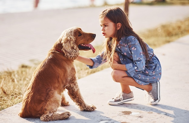 Cute little girl have a walk with her dog outdoors at sunny day