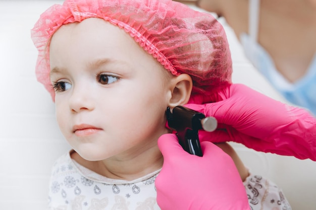 Cute little girl having ear piercing process with special piercing gun in beauty center by medical worker