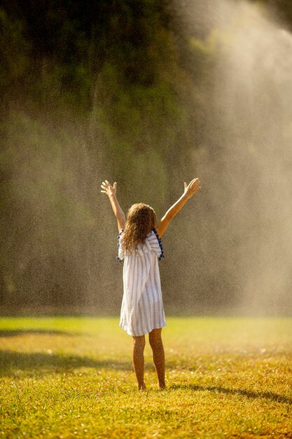 Cute little girl having fun with water under irrigation sprinkler