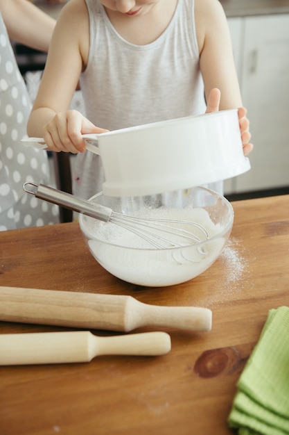 かわいい女の子は、お母さんがキッチンでクッキーを焼くのを手伝います。幸せな家族。調色。