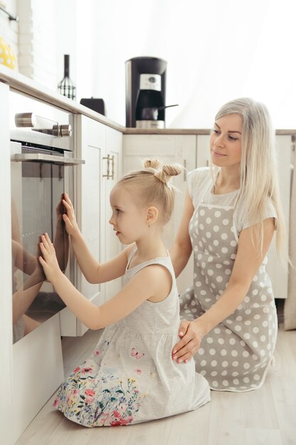 かわいい女の子は、お母さんがキッチンでクッキーを焼くのを手伝います。幸せな家族。調色。