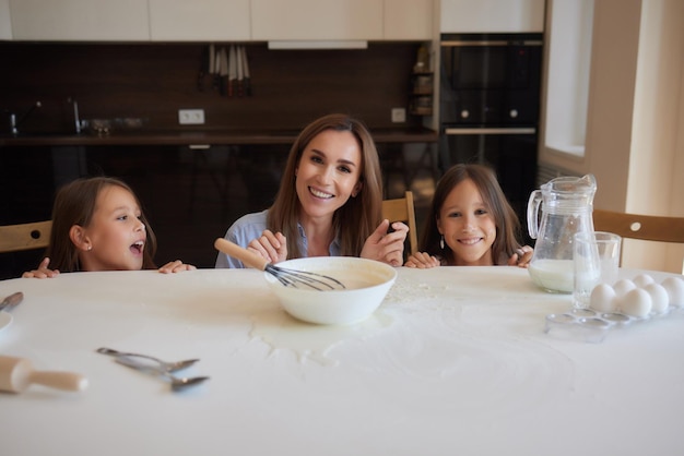 Cute little girl and her beautiful mom in aprons are playing and laughing while kneading the dough in the kitchen